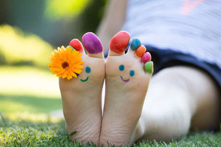 Child feet painted with colorful smiling face in green grassの写真素材