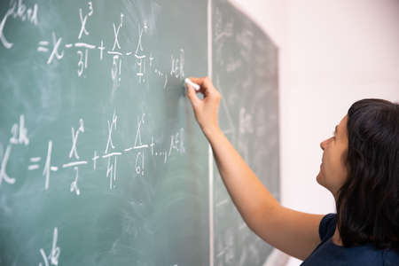 Teacher or student writing on blackboard during math lesson in school classroom.