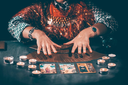 Fortune teller with tarot cards on table near burning candles.Tarot cards spread on table with...