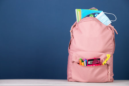 Backpack with school supplies and medical mask. Prevention while going back to school and new normal oncept.の写真素材