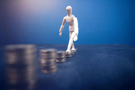 Wooden man wakling on increasing stacks of coins. Concept of hard work, financial growth.