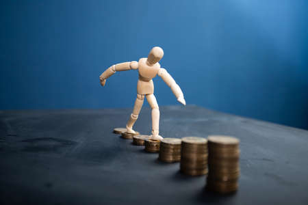 Wooden man wakling on increasing stacks of coins. Concept of hard work, financial growth.
