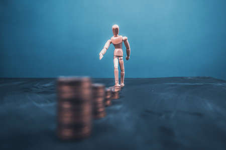Wooden man wakling on increasing stacks of coins. Concept of hard work, financial growth.の写真素材