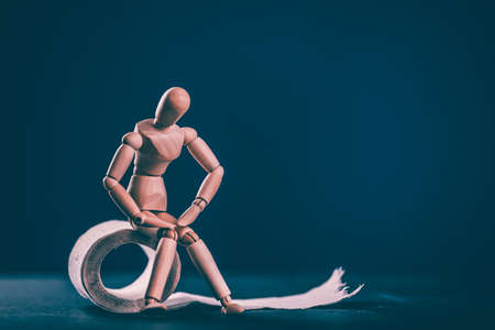 Wooden man with roll of toilet paper on blue background. Bowel problems, incontinence and diarrhea concept.の写真素材
