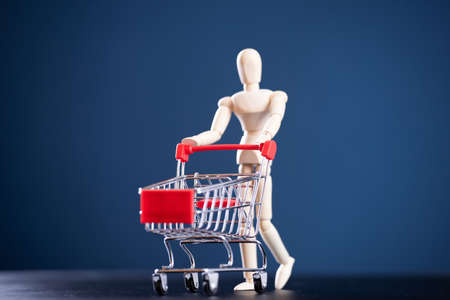Go shopping concept. Wooden figure with shopping cart on blue backgroundの写真素材