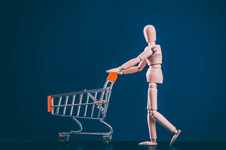 Go shopping concept. Wooden figure with shopping cart on blue backgroundの写真素材