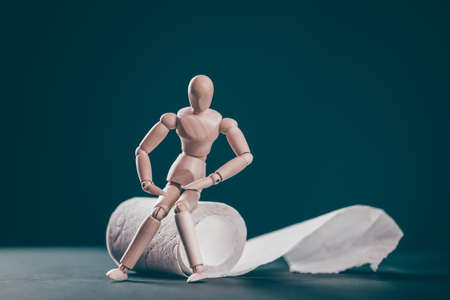 Wooden man with roll of toilet paper on blue background. Bowel problems, incontinence and diarrhea...