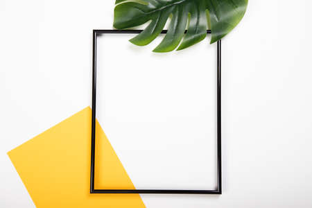 Photo frame with yellow paper blank and tropical palm leaves on white background. Flat lay with copy spaceの写真素材