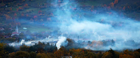 Evening view of picturesque village in the mountains surrounded by autumn mist and smoke. Fairy, magic rural landscape.の写真素材
