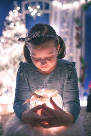Young girl holding a candy jar with homemade gingerbread cookies.Christmas lights on background