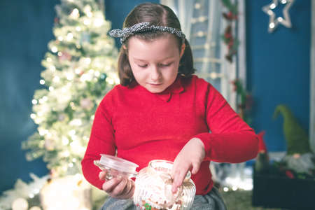 Young girl holding a candy jar with homemade gingerbread cookies.Christmas lights on backgroundの写真素材