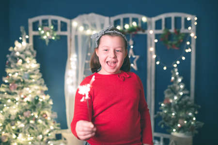 Young girl holding burning sparkler on festive holiday lights background. Christmas holidays,...