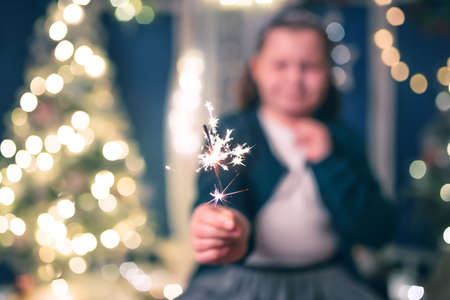 Young girl holding burning sparkler on festive holiday lights background. Christmas holidays, childhood and people conceptの写真素材