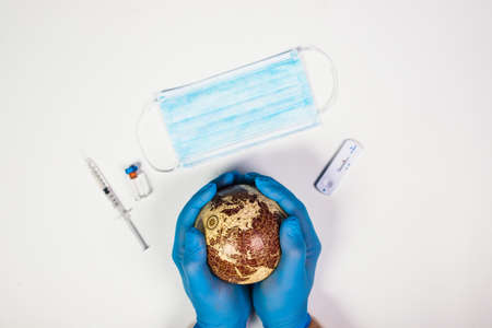 World epidemic danger concept. Hands of doctor holding planet Earth, vaccine, mask and test in the backgroundの写真素材