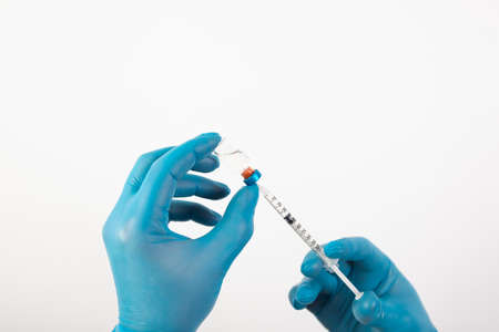 Vaccination concept. Doctor's hand in blue gloves hold medicine vaccine vial bottle and syringe.の写真素材