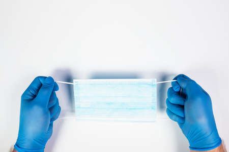 Doctor hand wear blue medical gloves holds antivirus face mask for pandemic diseases.の写真素材