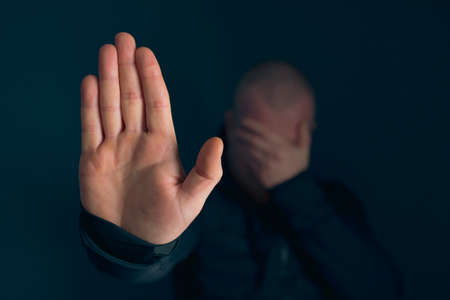 Sad, angry man showing stop sign on dark background. Low key photo.の写真素材