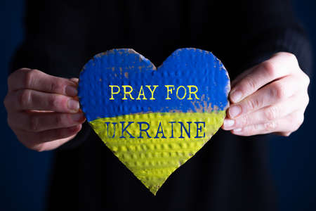 Heart shaped flag of Ukraine in female hands, Pray for Ukraine text.  The concept of solidarity with...