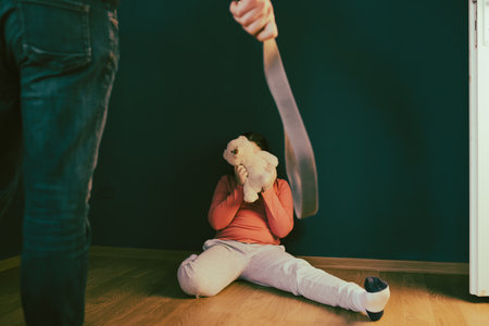 Child abuse, domestic violence concept. Mistreated little girl sitting on the floor being scared of an adult.の写真素材
