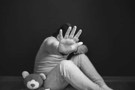 Child violence and abused concept. Little girl sitting in a dark room, showing stop sign