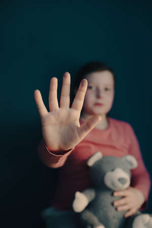 Child violence and abused concept. Little girl sitting in a dark room, showing stop sign