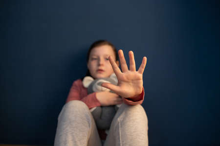 Child violence and abused concept. Little girl sitting in a dark room, showing stop signの写真素材