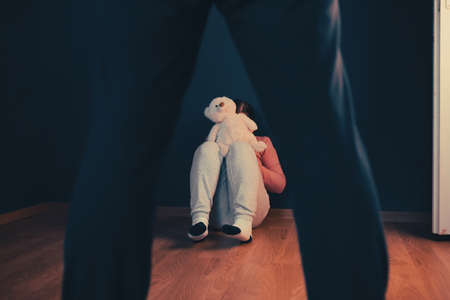 Child abuse, domestic violence concept. Mistreated little girl sitting on the floor being scared of an adult.の写真素材