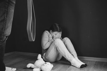 Child abuse, domestic violence concept. Mistreated little girl sitting on the floor being scared of an adult.の写真素材