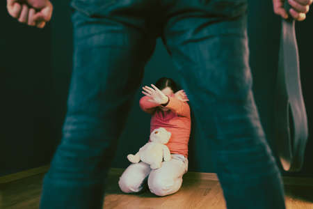 Child abuse, domestic violence concept. Mistreated little girl sitting on the floor being scared of an adult.の写真素材