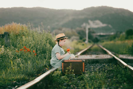 Retro styled photo of little girl with old luggage at the railwaysの写真素材
