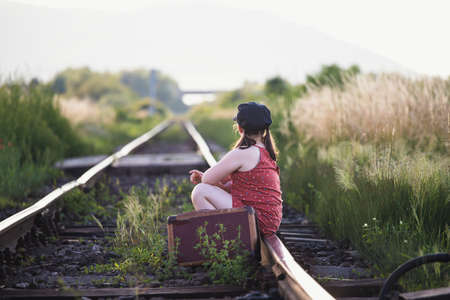 Retro styled photo of little girl with old luggage at the railwaysの写真素材