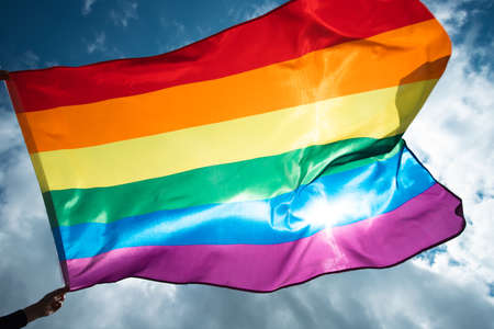 Bright rainbow LGBT flag fluttering against blue sky. LGBT community, happiness, freedom and love concept for same sex couples.の写真素材