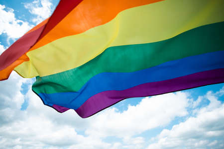 Bright rainbow LGBT flag fluttering against blue sky. LGBT community, happiness, freedom and love concept for same sex couples.の写真素材