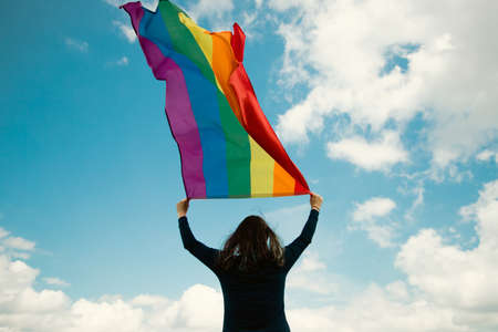 Woman sitting in a green meadow holding a Gay Rainbow Flag. Bisexual,gay, lesbian, transsexual symbol. Happiness, freedom and love concept for same sex couplesの写真素材