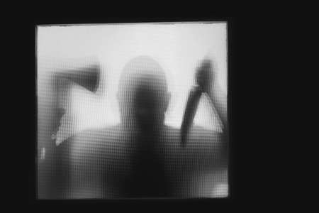 Horror, halloween background - Shadowy figure behind glass of a man holding an axe and a knifeの写真素材