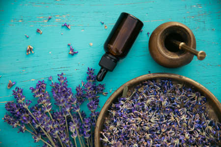 Flat lay of oil, bowl and bouquet of fresh lavender flowers on turquoise wooden background. Aromatherapy, spa, massage concept.の写真素材