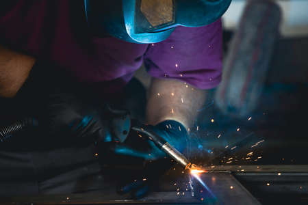 Handyman performing welding and grinding at his workplace in the workshop, while the sparks "fly" all around him. He is wearing a protective helmet and equipment.の写真素材