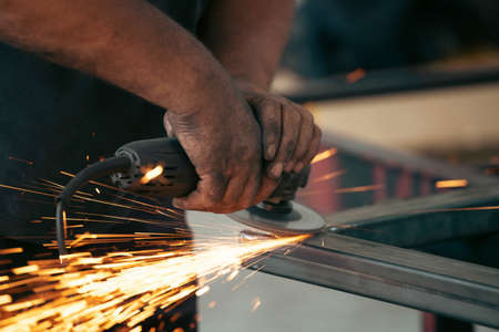 Profesional fabric worker cutting metal profile on the work table with an electric grinder in the industrial workshop.の写真素材