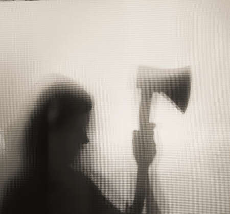 Horror, halloween background - Shadowy figure behind glass of a woman holding an axe