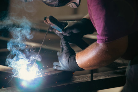 Handyman performing welding and grinding at his workplace in the workshop, while the sparks "fly" all around him. He is wearing a protective helmet and equipment.の写真素材