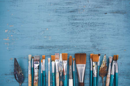 Artistic art supply utensils with paintbrushes on turquoise wooden background with copy space. Flat lay photoの写真素材