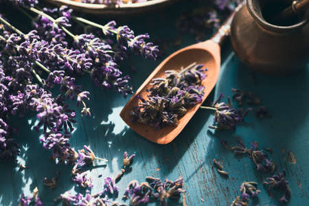 Flat lay of a bowl and wooden scoop of fresh lavender flowers on turquoise wooden background. Aromatherapy, spa, massage concept.の写真素材