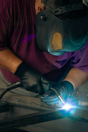 Handyman performing welding and grinding at his workplace in the workshop, while the sparks fly all...