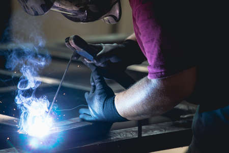 Handyman performing welding and grinding at his workplace in the workshop, while the sparks "fly" all around him. He is wearing a protective helmet and equipment.の写真素材