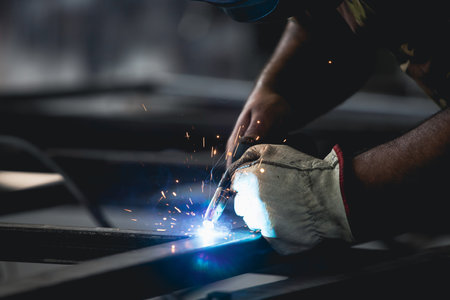 Handyman performing welding and grinding at his workplace in the workshop, while the sparks "fly" all around him. He is wearing a protective helmet and equipment.の写真素材