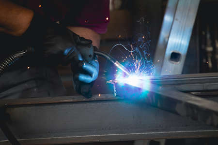 Handyman performing welding and grinding at his workplace in the workshop, while the sparks "fly" all around him. He is wearing a protective helmet and equipment.の写真素材