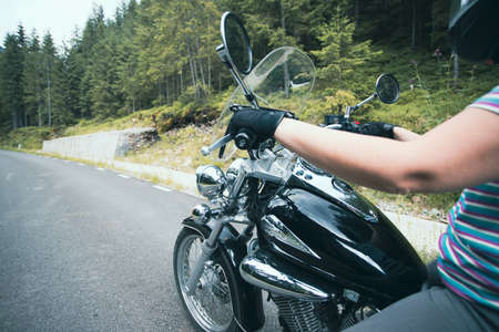 Close-up on the hands of a motorcycle driver riding on forest road. Travel and sport, speed and...