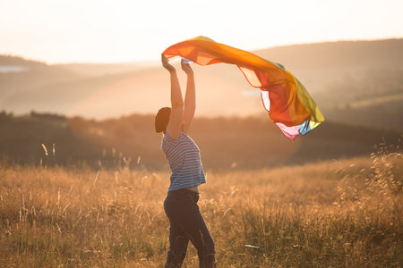 Woman holding a Gay Rainbow Flag in magic sunset. Happiness, freedom and love concept for same sex couplesの写真素材