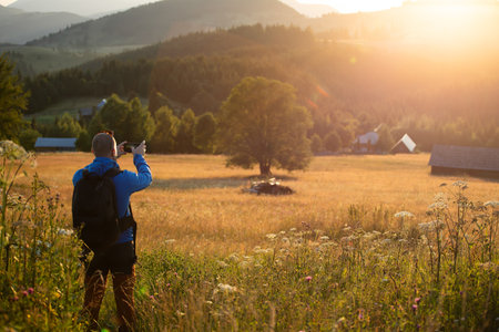 Male hiker in summer meadow looking at magic sunset over hills. Relaxation, nature and tourism concept.の写真素材