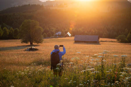Male hiker in summer meadow looking at magic sunset over hills. Relaxation, nature and tourism concept.の写真素材